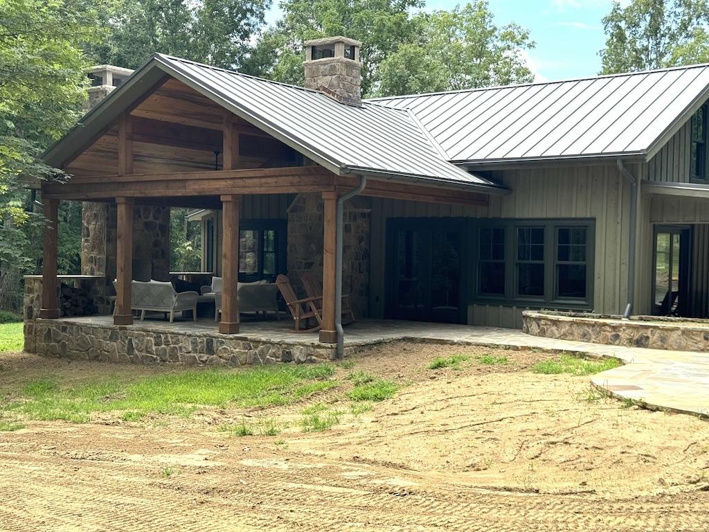 Photo of log home with green metal roof and open porch system with stone fireplace