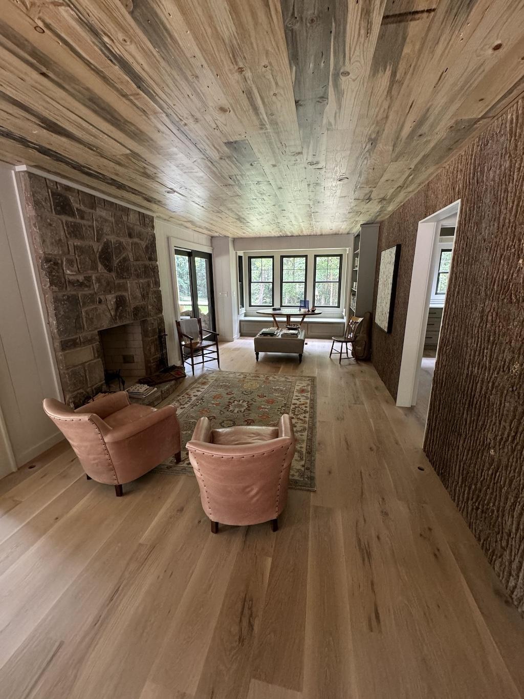 Living room space with 12 ft ceilings of exposed wood, hardwood floors and exposed wood walls. A floor to ceiling stone fireplace is a focal point of the room