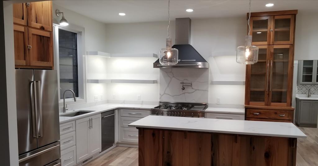 Photo of open kitchen with large island white marble countertops and honey wood cabinets with glass doors on upper storage