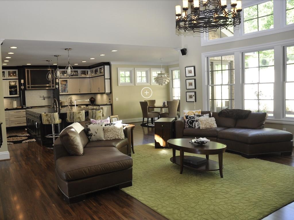 Photo of great room with open kitchen design. Soaring ceilings and large drop chandelier in great room. The exterior wall is windows