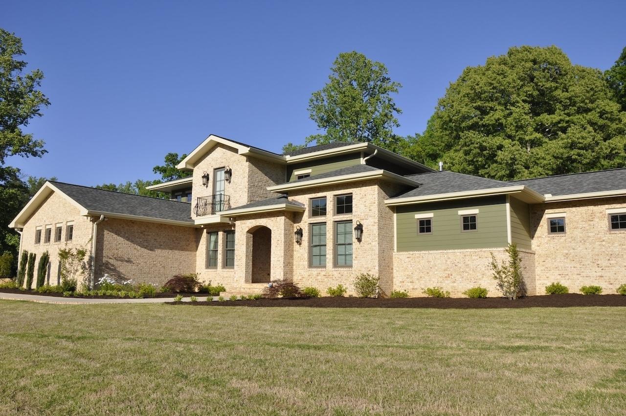 Photo of exterior of home with light brick facade and contrasted green painted upper dormers