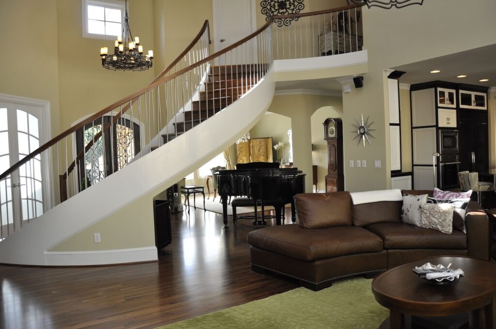 Photo of entry area and living room with open curved staircase leading to loft area. A grand piano is placed under the curved stairway